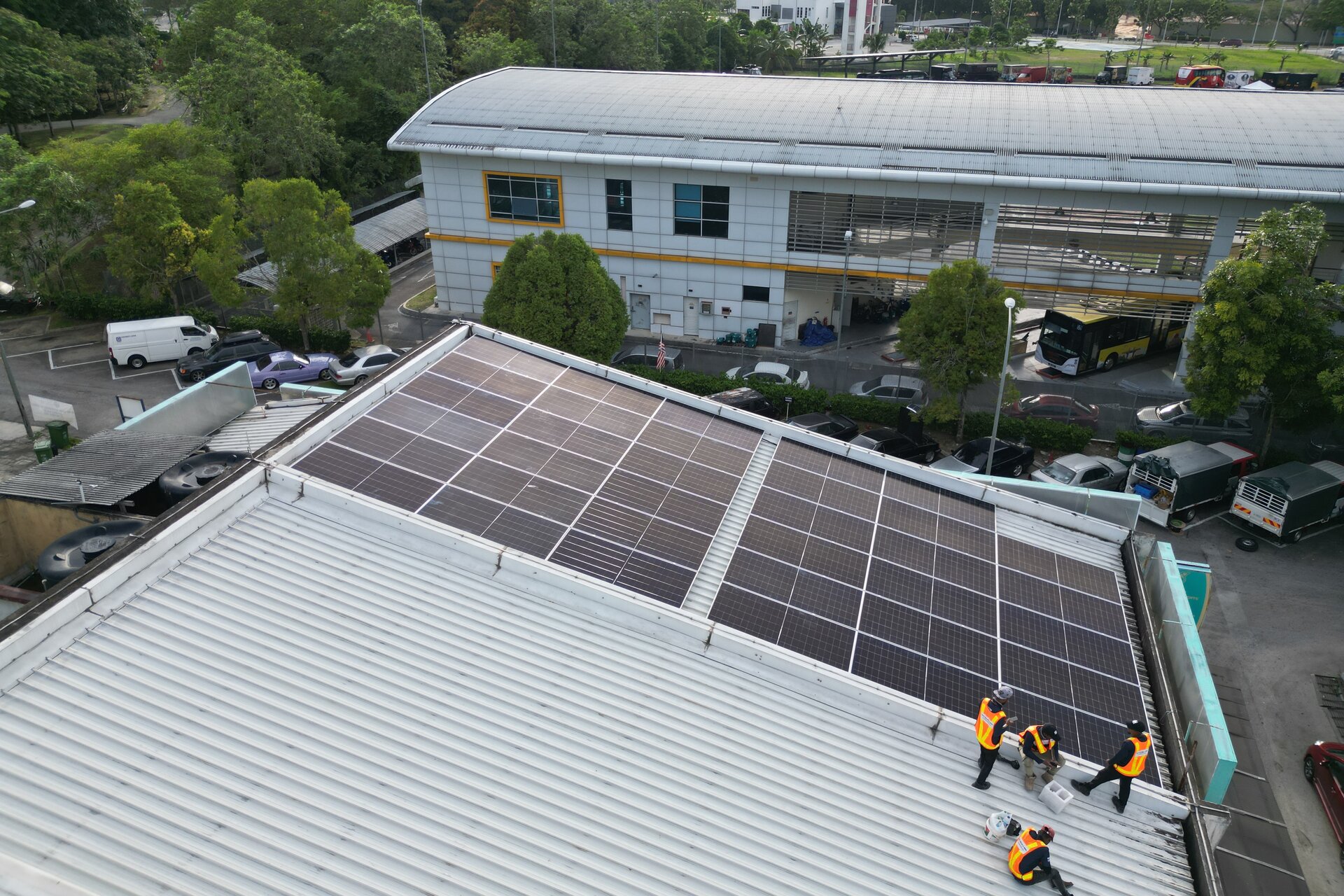 Aerial view of the RPG install team fitting a solar panel array on a commercial rooftop, with an industrial park in the background